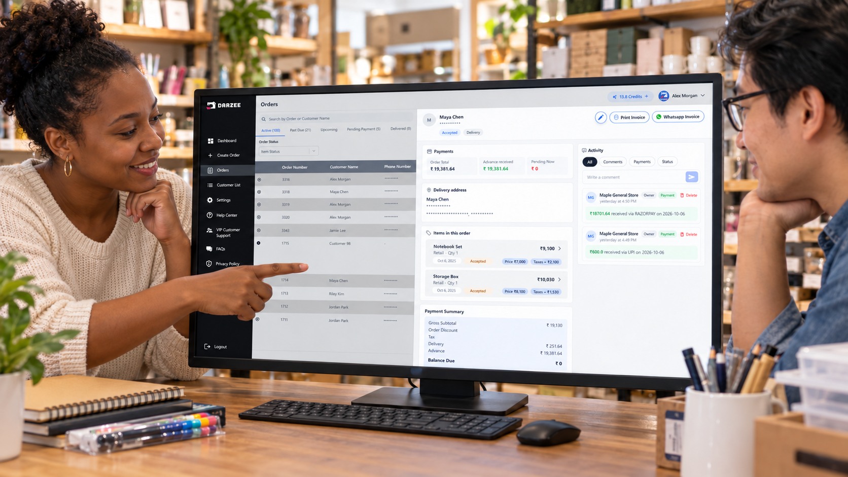 Two colleagues in everyday clothes reviewing a Darzee demo order on a large monitor in a stationery and home-goods store.
